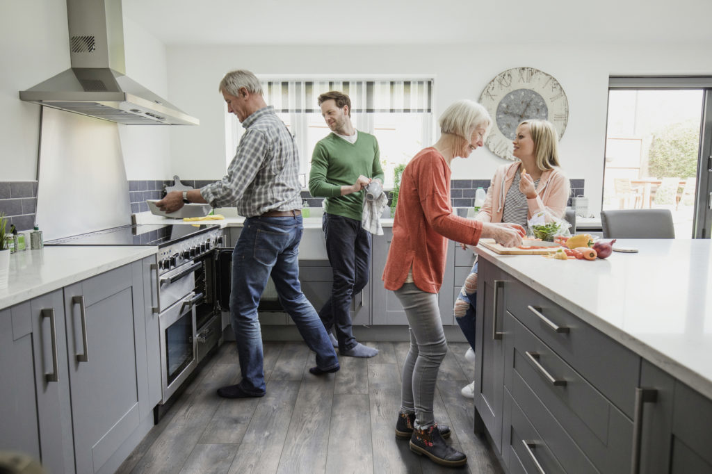 Siblings are helping their senior parents to cook a meal in their home while socialising.